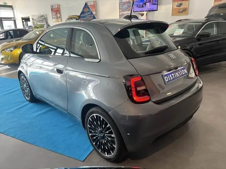 Fiat 500 électrique gris minéral métal vue 3/4 arrière droit en showroom avec jantes noires à rayons fins.