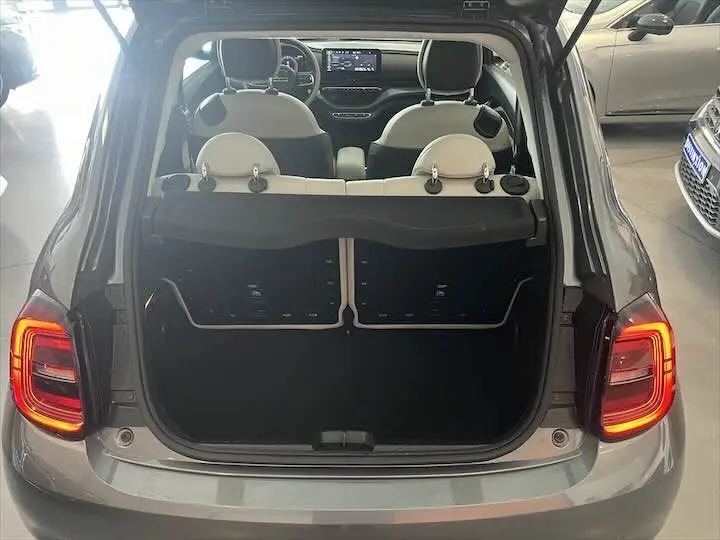 Vue arrière ouverte d'une Fiat 500 électrique gris minéral métal montrant le coffre vide et l'intérieur clair des sièges avant.
