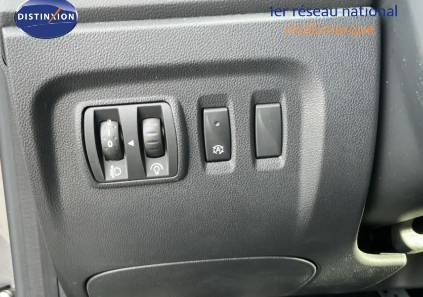 Gros plan sur les commandes de réglage des phares et du tableau de bord du Renault Captur gris, côté conducteur.