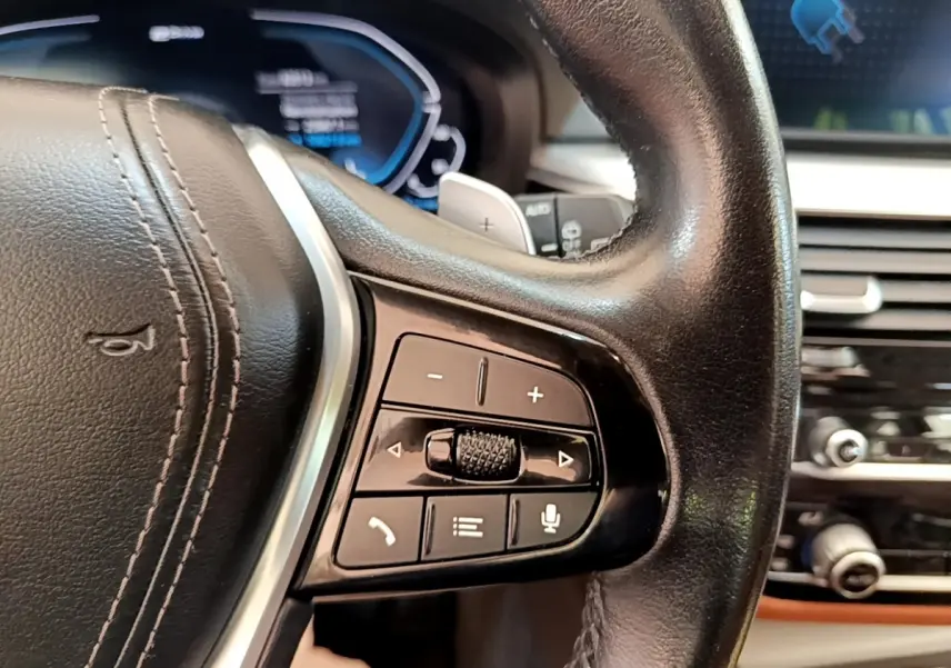 Gros plan sur le volant cuir noir de la BMW Série 5 Touring 530e 2022, avec commandes multifonctions et tableau de bord numérique.