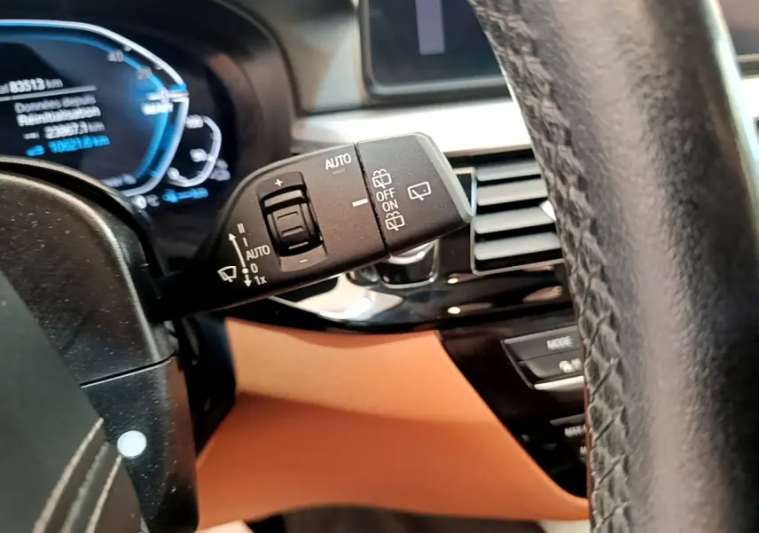 Gros plan sur la commande d’essuie-glace à gauche du volant cuir dans l’habitacle beige d’une BMW Série 5 Touring 530e.