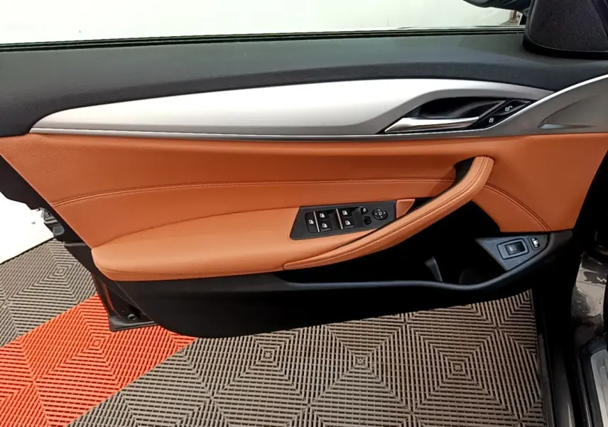 Gros plan sur la porte avant gauche intérieure de la BMW Série 5 Touring 530e avec garniture cuir marron et commandes électriques.