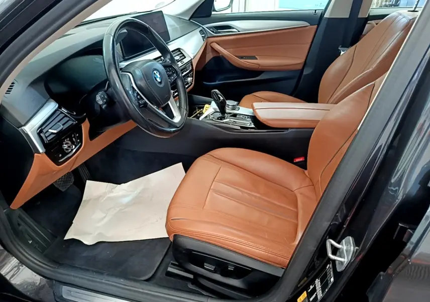 Vue intérieure côté conducteur de la BMW Série 5 Touring 530e 2022 avec sièges cuir marron et tableau de bord gris clair.