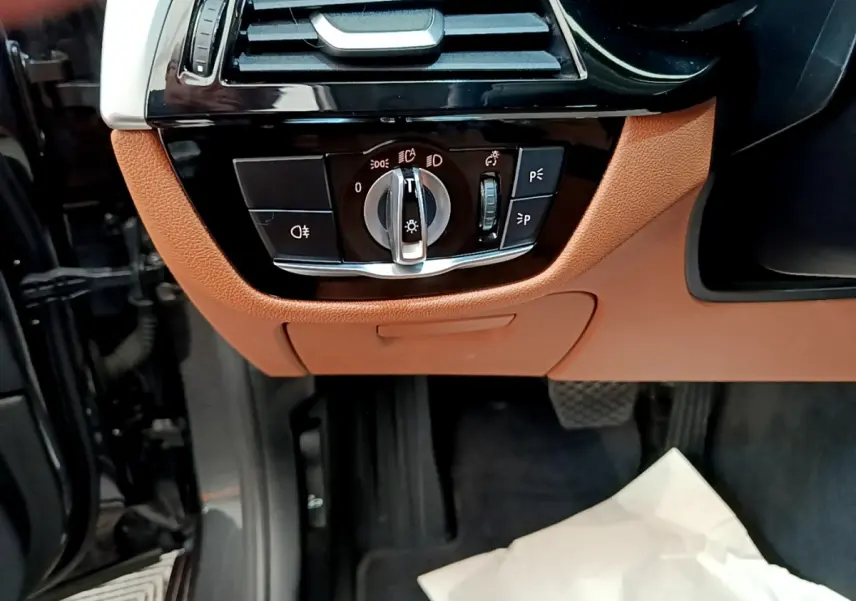 Détail intérieur du panneau de commande des phares sur tableau de bord marron clair d'une BMW Série 5 Touring 530e.