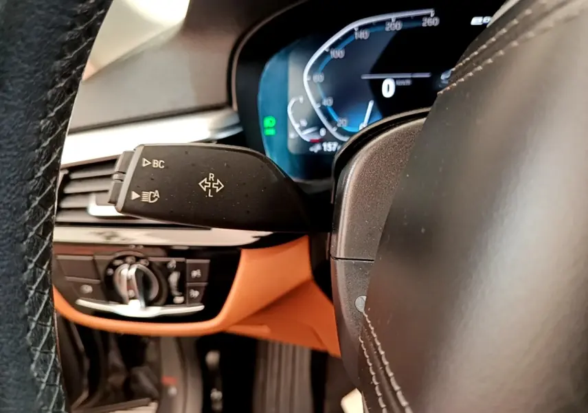 Gros plan sur le volant noir et le tableau de bord numérique bleu de la BMW Série 5 Touring 530e 2022.