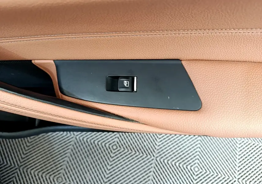Gros plan sur le bouton de commande de la vitre dans la portière en cuir marron clair d’une BMW Série 5 Touring 530e 2022.