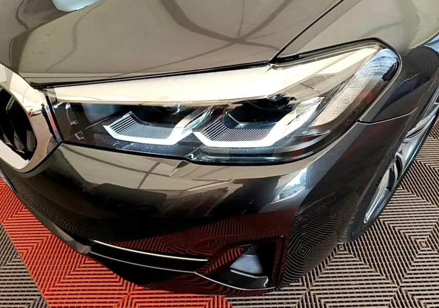Gros plan sur le phare avant droit d'une BMW Série 5 Touring gris clair avec détails LED et calandre partielle visible.