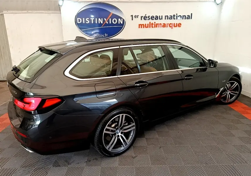 BMW Série 5 Touring 530e gris clair vue 3/4 arrière droit, avec jantes alliage et feux arrière LED allumés.
