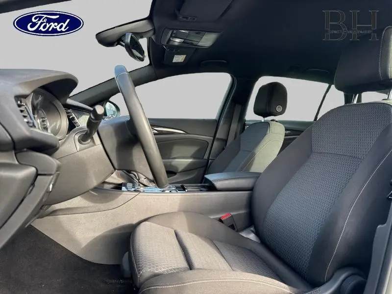 Vue intérieure côté conducteur de l’Opel Insignia Sports Tourer 1.5 D Elegance Business avec sièges tissu noir et volant cuir multifonction.