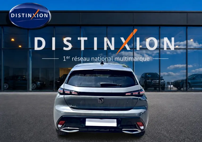 Vue arrière d'une Peugeot 308 gris métallisé 2025 garée devant une vitrine avec logo Distinxion.