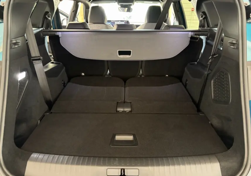 Coffre ouvert en vue arrière d’un Peugeot 5008 vert avec banquette arrière rabattue et cache-bagages déployé.