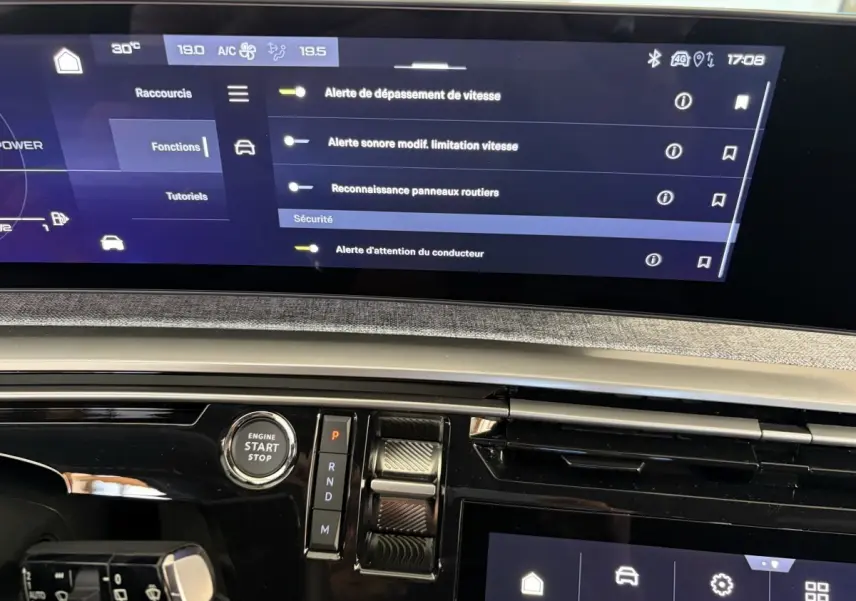 Vue rapprochée du tableau de bord numérique et console centrale du Peugeot 5008 Hybrid vert, avec écran tactile et bouton start/stop.