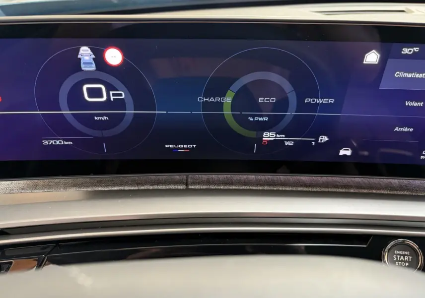 Tableau de bord numérique du Peugeot 5008 hybride, affichage multifonctions avec indicateurs de charge et vitesse, bouton start visible.