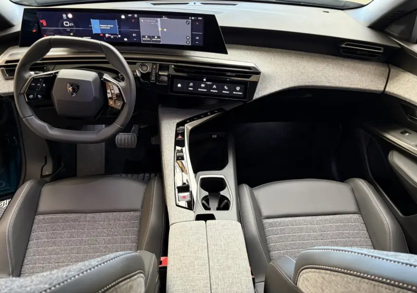 Vue intérieure avant du Peugeot 5008 Hybrid 2025, tableau de bord moderne avec écran large et sièges gris tissu et cuir.
