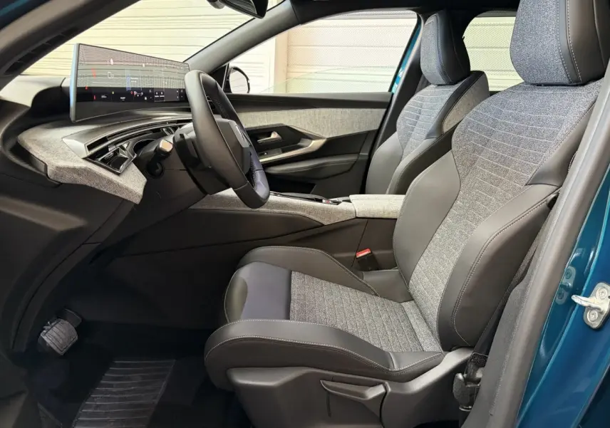 Vue intérieure côté conducteur du Peugeot 5008 Hybrid 145 avec sièges tissu et cuir gris, tableau de bord numérique et portière bleu visible.