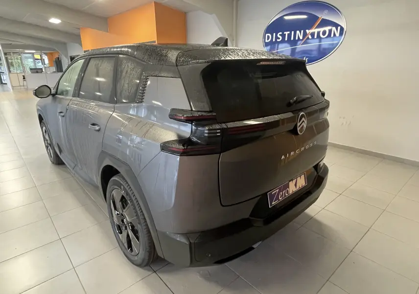 Vue 3/4 arrière d'un Citroën C5 Aircross hybride gris platinium avec toit noir dans un showroom intérieur.