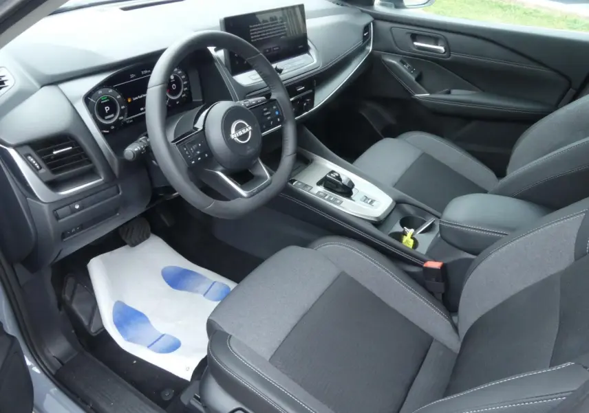 Intérieur avant du Nissan Qashqai 2025 gris, vue côté conducteur sur tableau de bord et sièges tissu noir et gris.