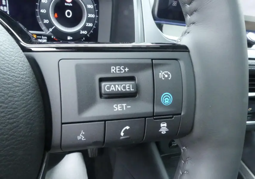 Gros plan sur les commandes du volant cuir noir du Nissan Qashqai gris métallisé, affichage numérique en arrière-plan.