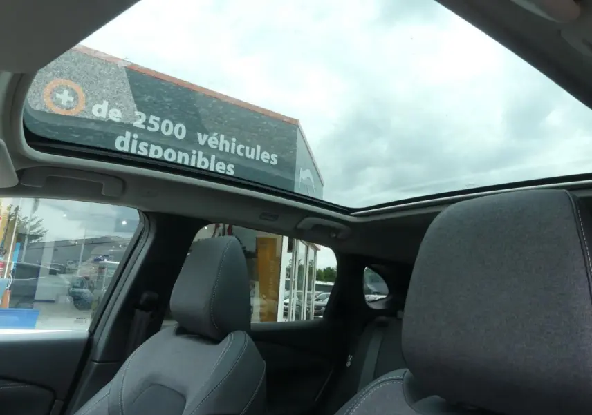 Intérieur du Nissan Qashqai 2025 gris métallisé, vue sur les sièges avant et toit panoramique en verre ouvert.