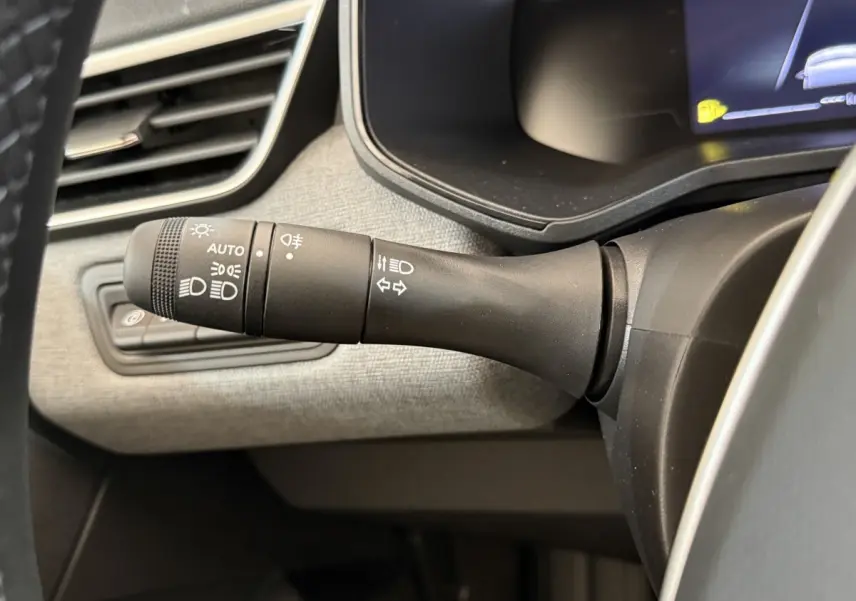Gros plan sur la commande des phares et clignotants à gauche du volant dans l’habitacle gris clair d’une Renault Clio noire 2025.