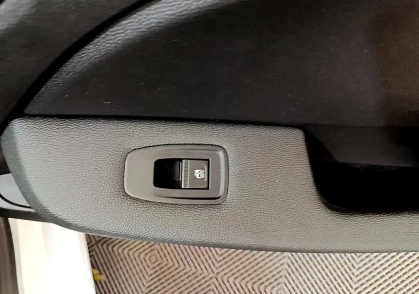 Gros plan sur le bouton de commande de la vitre électrique côté conducteur dans l'habitacle noir d'une Renault Clio blanche 2020.