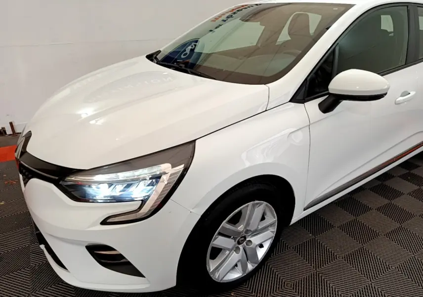 Renault Clio Business TCe 100 blanche vue en 3/4 avant droit avec phares LED allumés et jantes alliage.