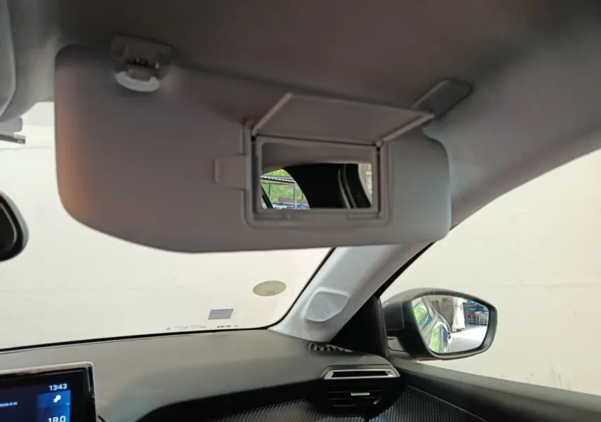 Intérieur de la Peugeot 208 BlueHDi 100, vue côté passager avec pare-soleil et miroir éclairé ouvert.