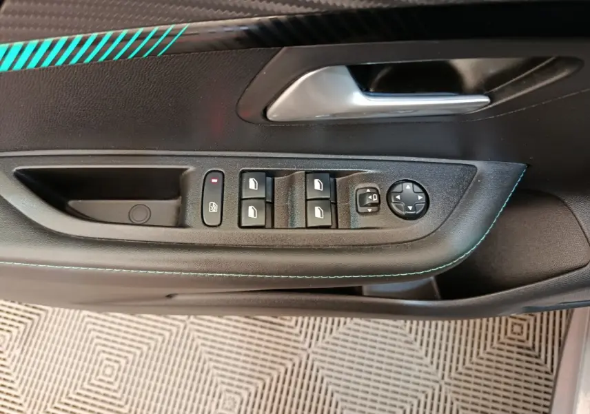 Vue rapprochée de la porte côté conducteur d’une Peugeot 208 avec commandes de vitres et rétroviseurs, surpiqûres bleues visibles.