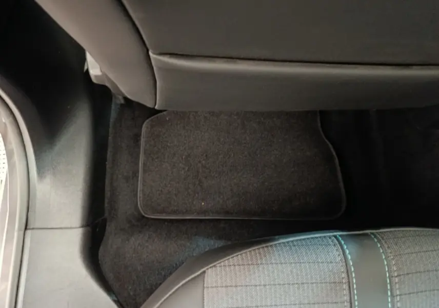 Vue intérieure du plancher arrière côté droit d'une Peugeot 208 2020 avec tapis de sol noir et siège tissu gris à surpiqûres bleues.