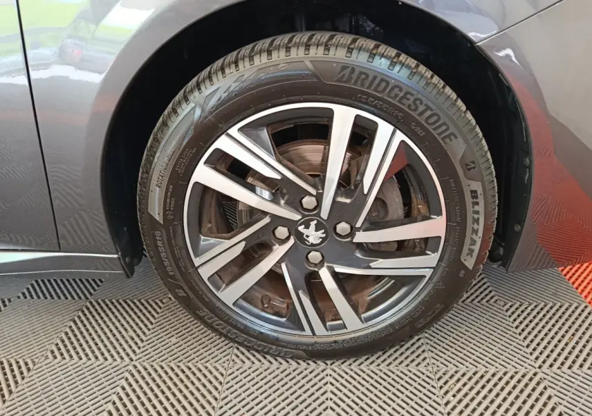 Gros plan sur la roue avant gauche grise d'une Peugeot 208 avec jante alliage et pneu Bridgestone Blizzak.