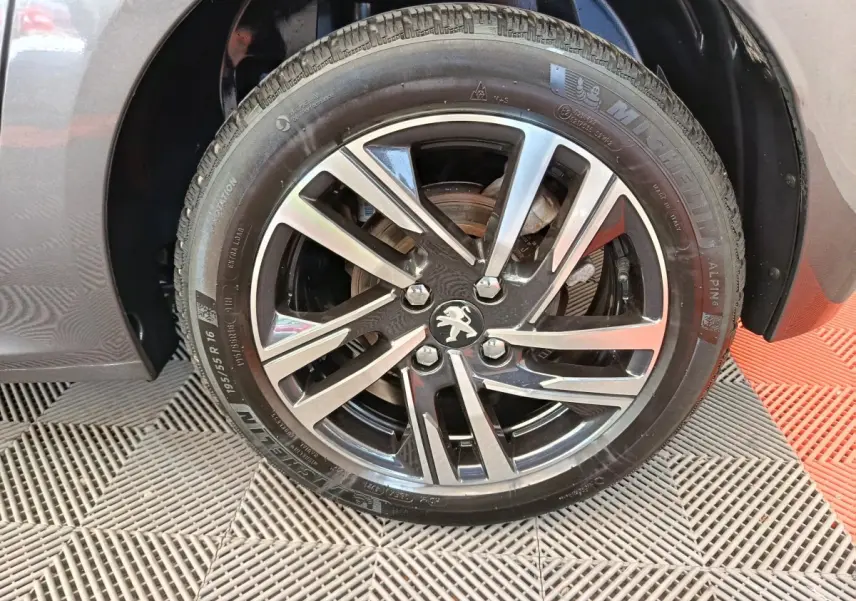 Gros plan sur la roue avant droite d'une Peugeot 208 gris métallisé avec jante alliage noire et argentée.