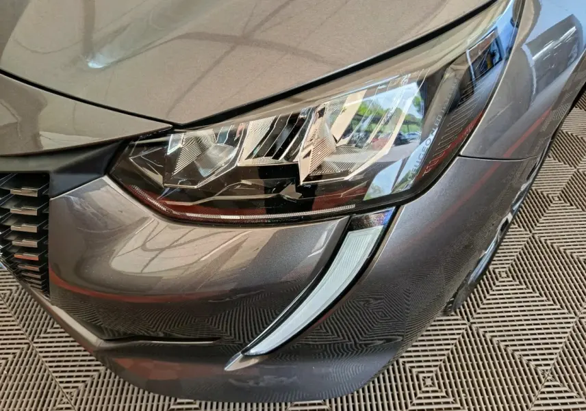 Gros plan sur le phare avant droit gris métallisé d'une Peugeot 208 avec signature lumineuse LED distinctive.