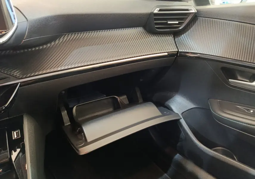 Intérieur côté passager de la Peugeot 208 2020 avec boîte à gants ouverte et tableau de bord noir à effet carbone.