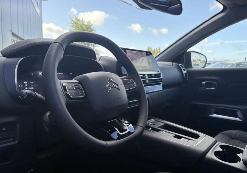 Vue intérieure côté conducteur du Citroën C5 Aircross 2025, tableau de bord et volant noirs avec écran tactile central.