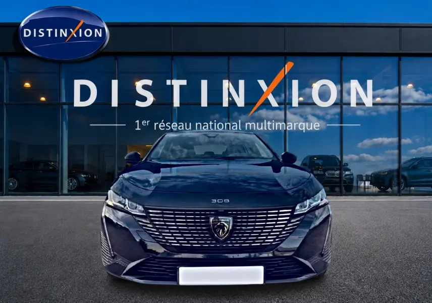 Vue frontale d'une Peugeot 308 noire 2025 avec calandre distinctive et logo lion au centre, devant une vitrine Distinxion.