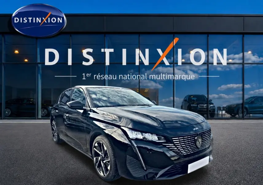 Peugeot 308 noire vue en 3/4 avant droit devant une vitrine Distinxion, avec jantes alu et phares LED allumés.