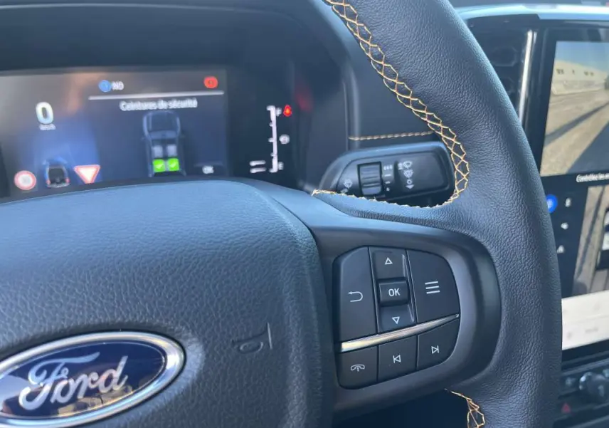 Gros plan sur le volant cuir noir avec surpiqûres jaunes du Ford Ranger 2026, tableau de bord numérique en arrière-plan.