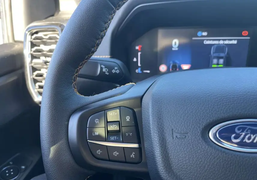 Gros plan sur le volant en cuir noir du Ford Ranger 2026, avec commandes multifonctions et tableau de bord numérique en arrière-plan.