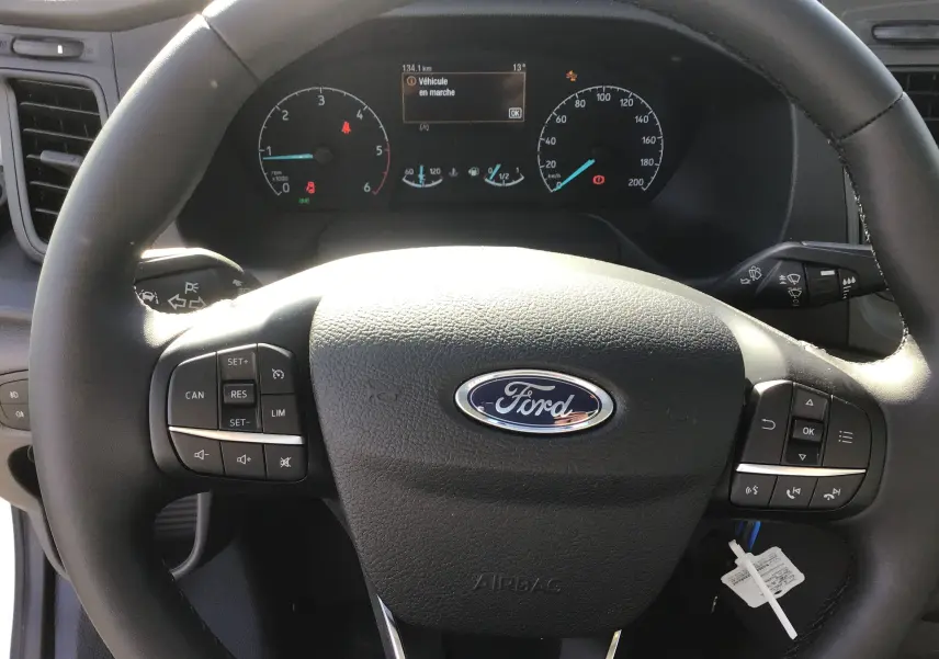 Vue rapprochée du volant Ford avec commandes intégrées et tableau de bord numérique du Transit Chassis Cabine blanc.