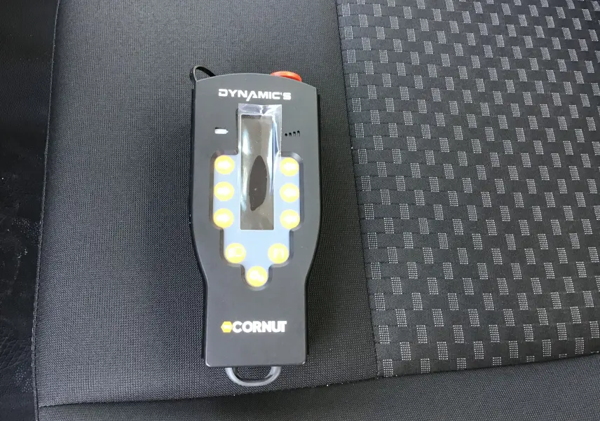 Télécommande noire du bras Polybenne Cornut posée sur un siège tissu gris foncé à motifs du Ford Transit Chassis Cabine blanc.