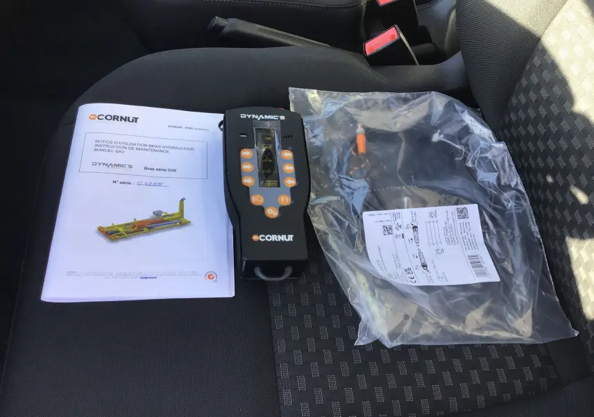 Vue intérieure du siège avant droit d'un Ford Transit blanc avec manuel, télécommande et câble du bras polybenne Cornut.