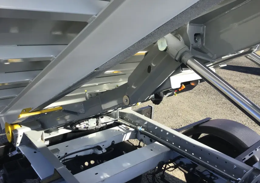 Gros plan sur le mécanisme de levage hydraulique du bras polybenne du Ford Transit blanc vu côté arrière droit.