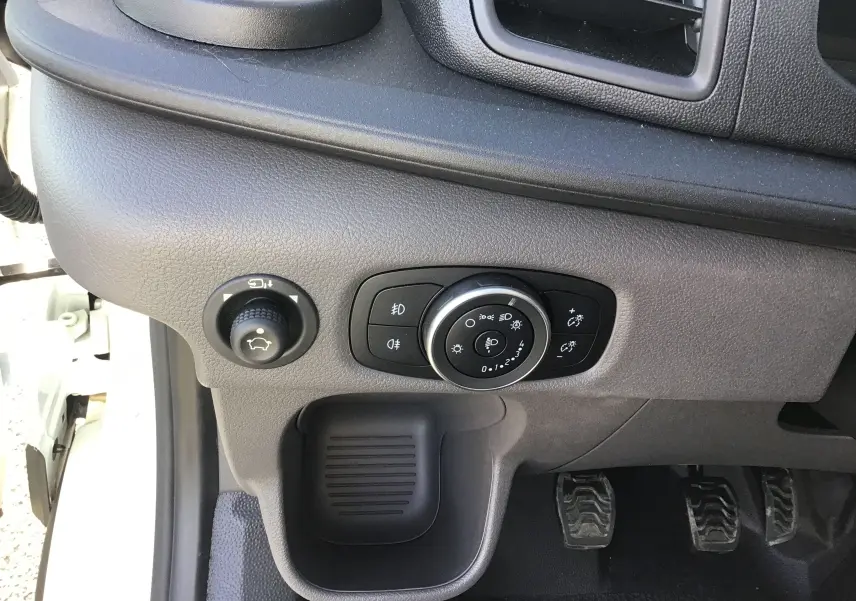 Vue rapprochée du tableau de bord côté gauche du Ford Transit Chassis Cabine blanc, avec commandes d'éclairage et pédales visibles.