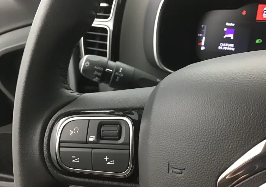 Gros plan sur les commandes du volant cuir noir d'un Citroën C5 Aircross gris Artense, avec tableau de bord numérique en arrière-plan.