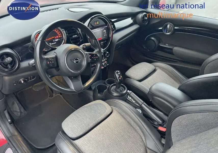 Vue intérieure côté conducteur de la MINI Cabriolet rouge chili 2023, avec tableau de bord moderne et sièges tissu-cuir gris.