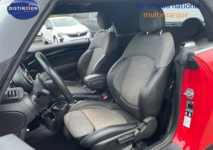 Vue intérieure côté conducteur d'une MINI Cabriolet F57 rouge chili, sièges tissu gris et cuir noir, volant et tableau de bord visibles.