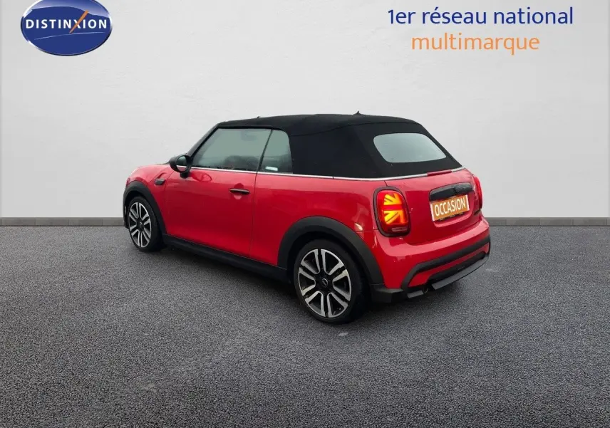 Vue 3/4 arrière droite d'une MINI Cabriolet rouge chili avec toit noir fermé et jantes bi-ton sur sol gris.