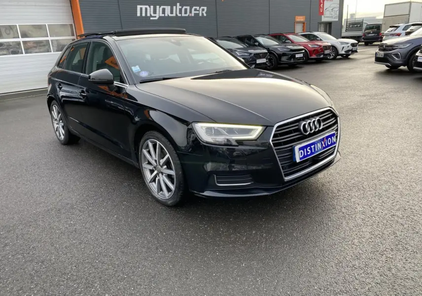 Audi A3 Sportback noir vue 3/4 avant droit, avec phares LED allumés sur parking extérieur.