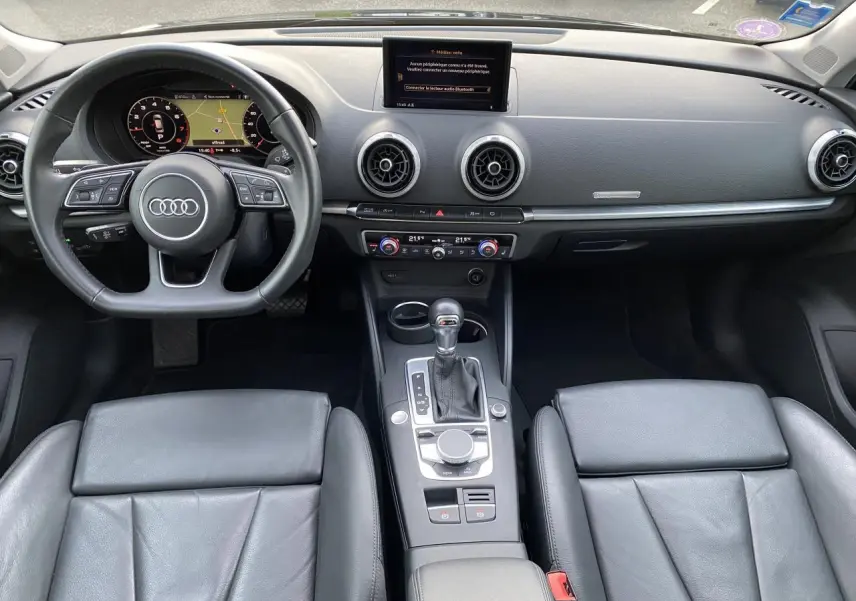 Vue intérieure avant de l'Audi A3 Sportback 2019, tableau de bord noir avec volant multifonction et console centrale moderne.
