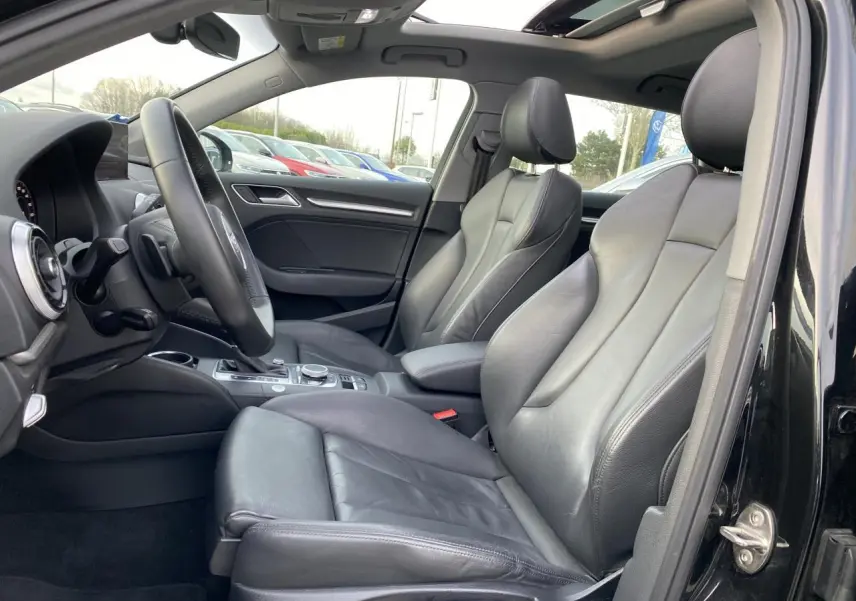 Vue intérieure côté conducteur de l'Audi A3 Sportback noire, montrant les sièges sport en cuir Milano et le toit panoramique en verre.